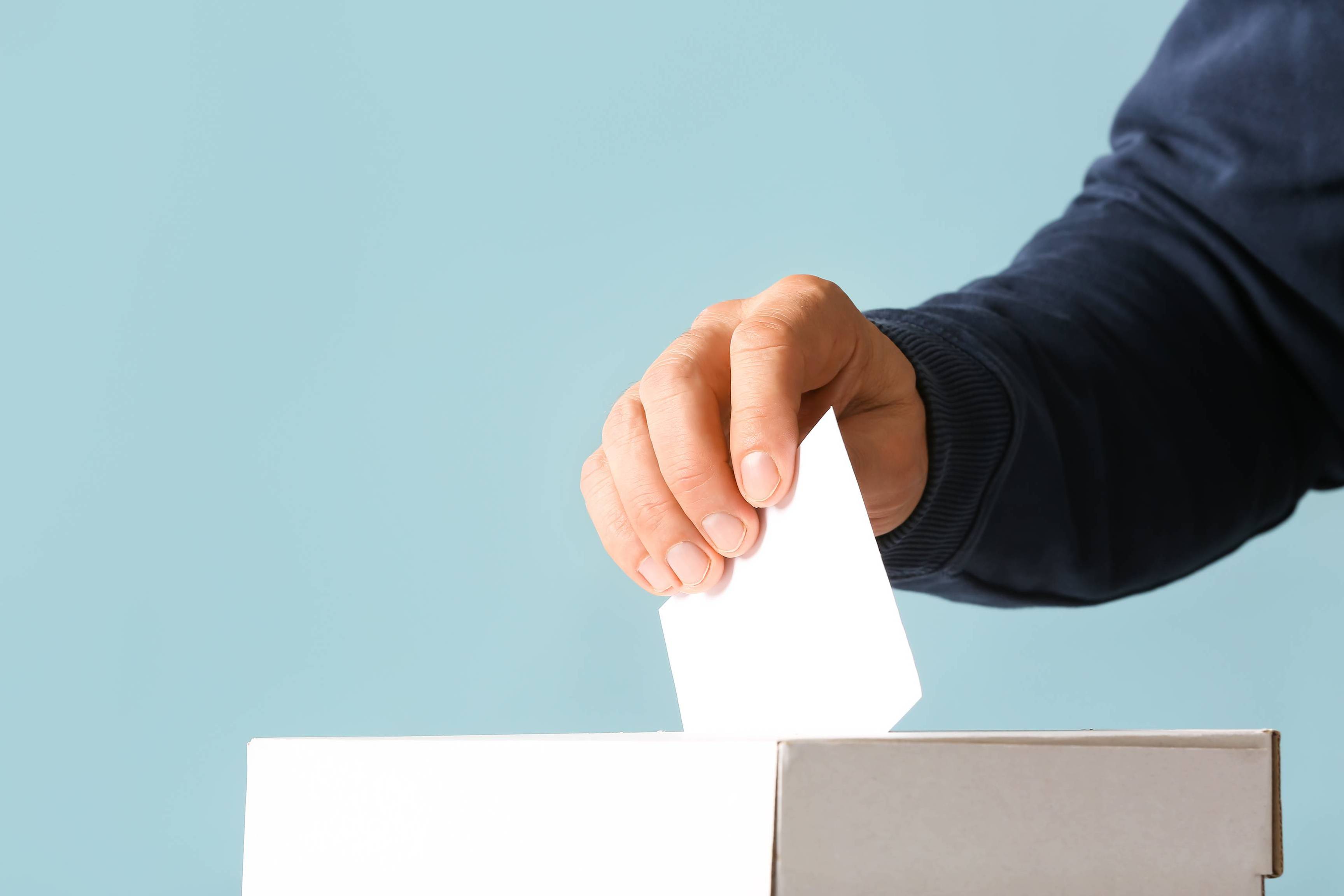 Voting man near ballot box on color background
